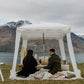 Couple sitting on cushions enjoying a picnic under a white canopy with a ‘Will you marry me?’ sign beside them.