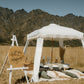 Romantic picnic setup with a table, pillows, white canopy and a ‘Will you marry me?’ sign in a mountain field.