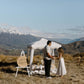Man proposing to his girlfriend on a mountain, with a romantic picnic set up behind them