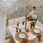 Beautifully styled picnic table outdoors with a white tablecloth and luxury place settings.