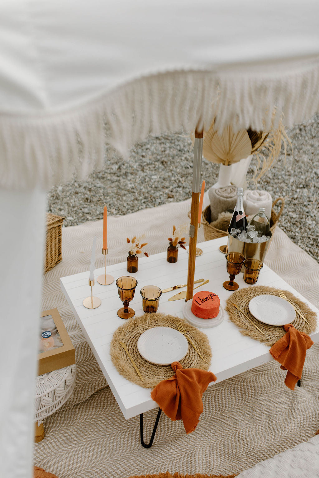 Beautifully styled picnic table outdoors with a white tablecloth and luxury place settings.