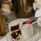 Chocolate cake with white frosting and floral decorations on a marble stand.