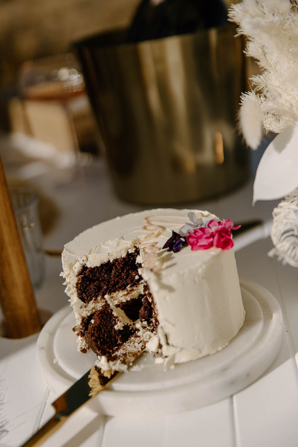 Chocolate cake with white frosting and floral decorations on a marble stand.