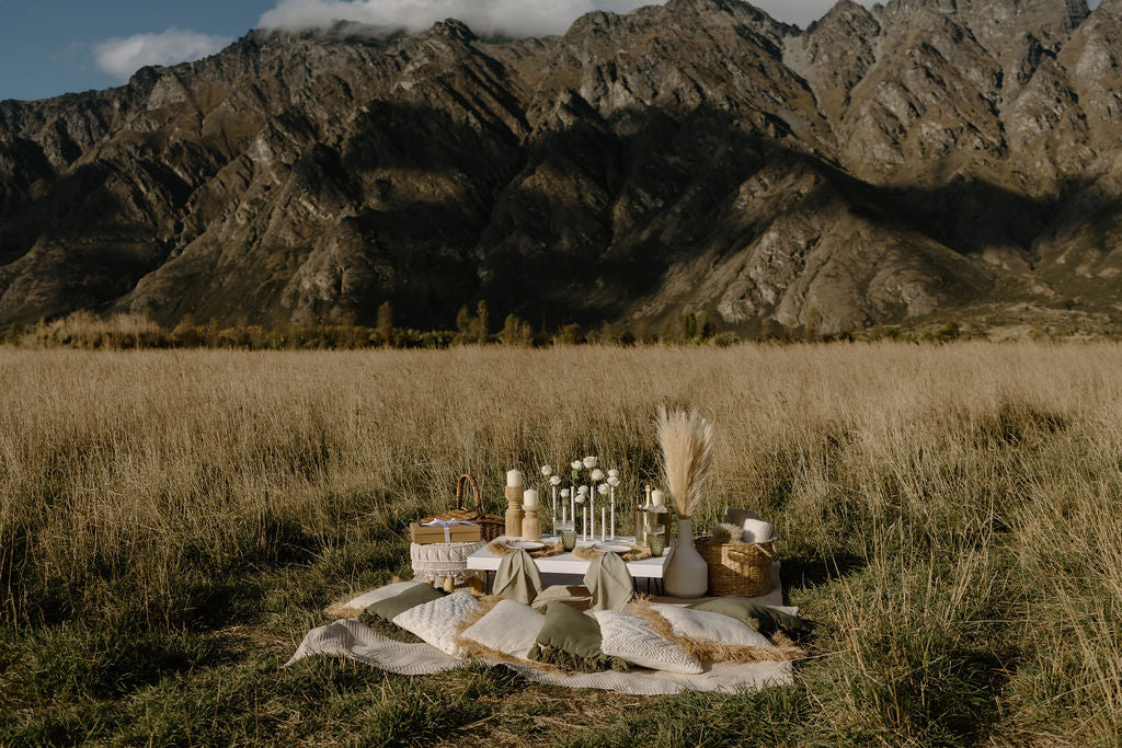 Romantic picnic setup with table and decorations in a field with mountains in the background